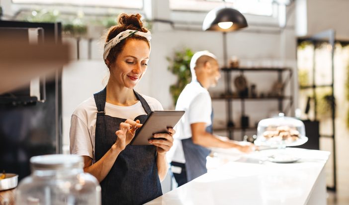 Cafe waitress using a digital tablet to manage orders. Woman using a touchscreen device that helps her to view and organize orders effectively, ensuring prompt and efficient service for the customers.
